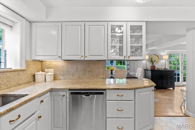 kitchen featuring dishwasher, white cabinets, light stone countertops, glass insert cabinets, and tasteful backsplash