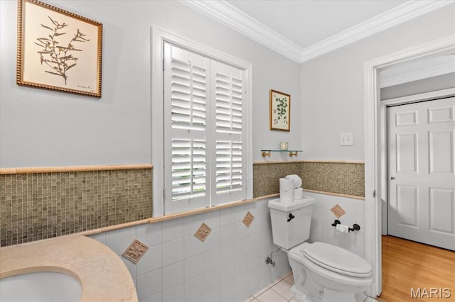 half bath featuring tile walls, toilet, ornamental molding, and wainscoting