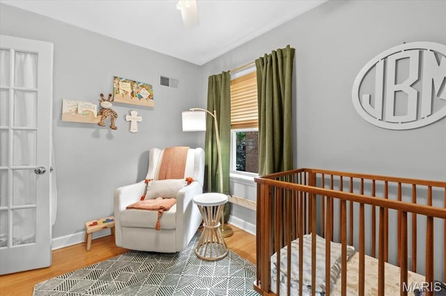 bedroom featuring wood finished floors, a nursery area, baseboards, and a ceiling fan