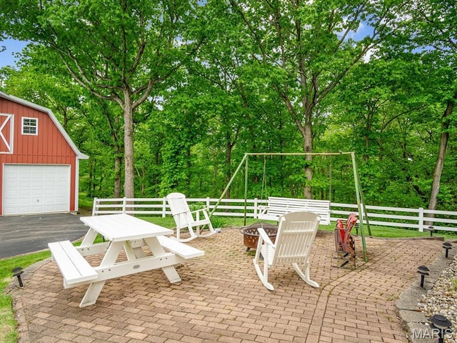view of patio / terrace featuring an outdoor fire pit, fence, an outbuilding, view of scattered trees, and a garage