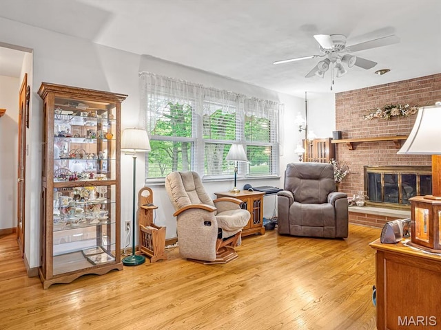 sitting room featuring wood finished floors, ceiling fan, and a brick fireplace