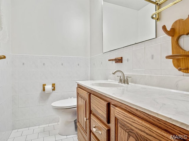bathroom featuring tile walls, toilet, vanity, and wainscoting