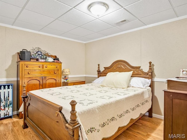 bedroom with light wood-style flooring, ornamental molding, a drop ceiling, and baseboards