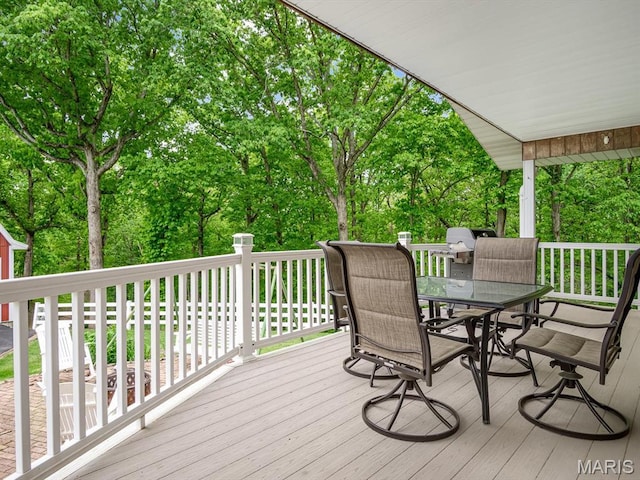 wooden deck with outdoor dining area, view of wooded area, and area for grilling