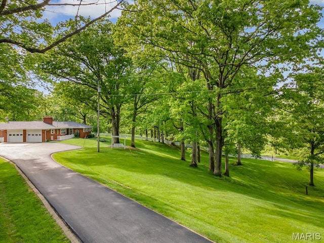 view of home's community featuring an attached garage, asphalt driveway, a yard, and view of wooded area