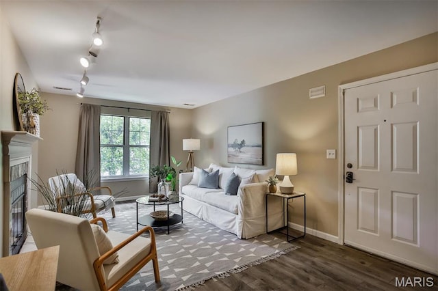 living area with a tiled fireplace, wood finished floors, rail lighting, and baseboards