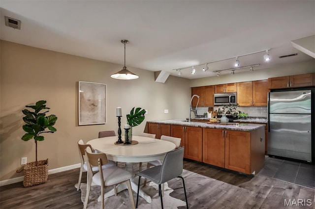 kitchen with appliances with stainless steel finishes, brown cabinets, dark wood-style flooring, decorative backsplash, and decorative light fixtures