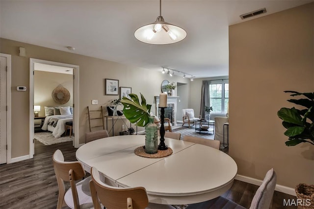 dining area with rail lighting, baseboards, wood finished floors, and a glass covered fireplace