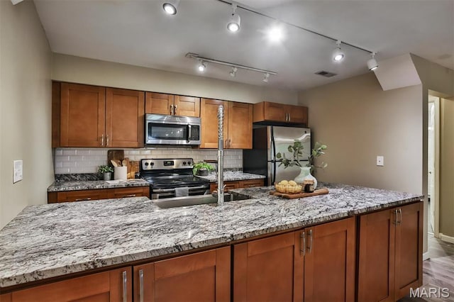 kitchen featuring appliances with stainless steel finishes, brown cabinetry, tasteful backsplash, light stone countertops, and light wood finished floors