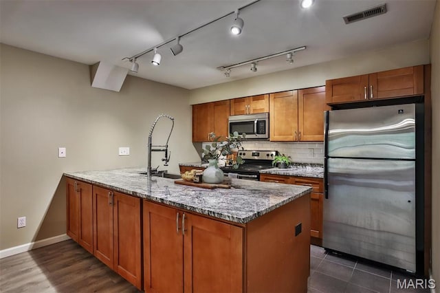 kitchen featuring appliances with stainless steel finishes, brown cabinets, a peninsula, light stone counters, and decorative backsplash