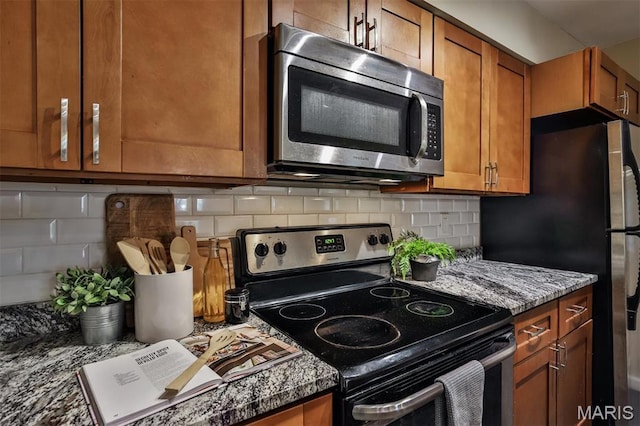 kitchen with stainless steel appliances, brown cabinets, tasteful backsplash, and dark stone counters