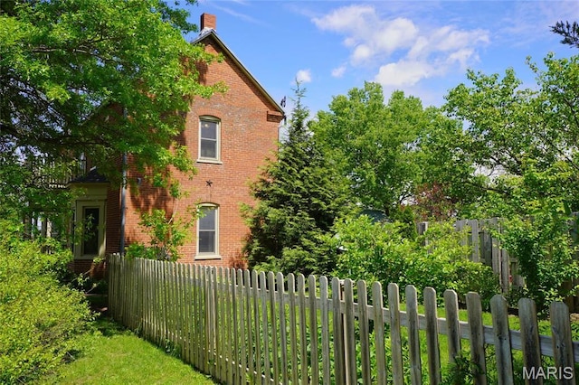 view of home's exterior with brick siding, fence, and a chimney