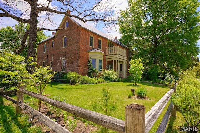view of side of property with a balcony, a chimney, brick siding, and a yard