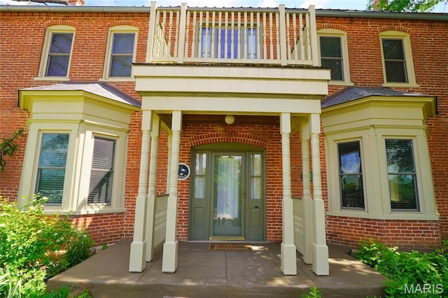 property entrance with a balcony, brick siding, and a porch