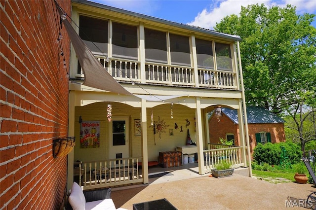back of property featuring a patio, brick siding, covered porch, and a balcony
