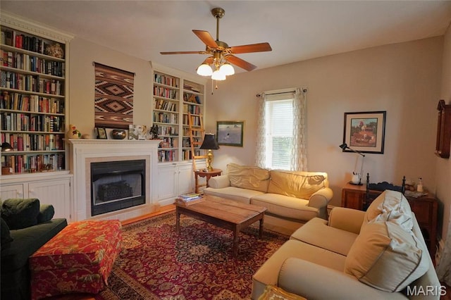living room featuring a ceiling fan, a fireplace, and built in features