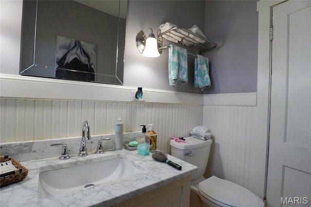 half bath featuring a wainscoted wall, toilet, and vanity