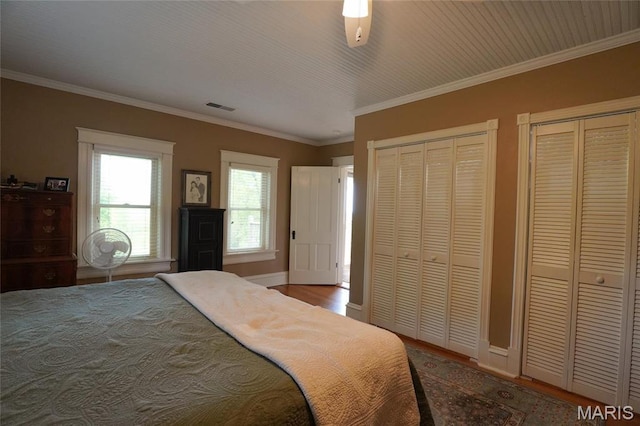 bedroom with two closets, wood finished floors, baseboards, crown molding, and a ceiling fan