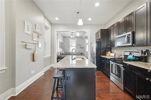 3015 Indiana Ave, Saint Louis, MO 63118 - kitchen featuring stainless steel appliances, a sink, a breakfast bar area, ceiling fan, and light stone counters