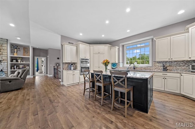 111 Foristell Ridge Ct, Foristell, MO 63348 - kitchen with double oven, a kitchen bar, a center island, backsplash, and light wood-style floors