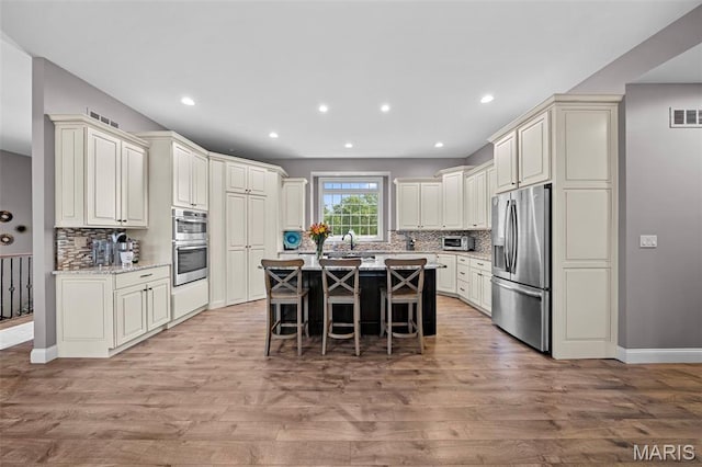 111 Foristell Ridge Ct, Foristell, MO 63348 - kitchen with appliances with stainless steel finishes, backsplash, light wood-style floors, a kitchen breakfast bar, and recessed lighting