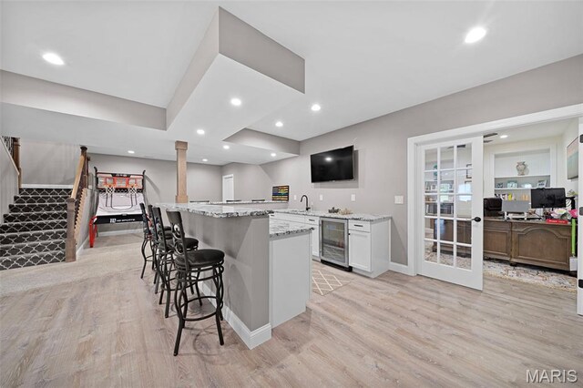 111 Foristell Ridge Ct, Foristell, MO 63348 - kitchen with beverage cooler, light wood-type flooring, a breakfast bar area, light stone countertops, and baseboards