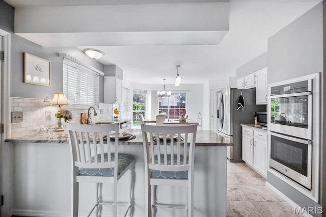 300 Wildberry Ln, Saint Charles, MO 63304 - kitchen featuring appliances with stainless steel finishes, a chandelier, white cabinetry, decorative backsplash, and a breakfast bar