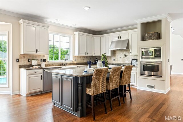 5316 Enchanted Ct, Weldon Spring, MO 63304 - kitchen with stainless steel appliances, under cabinet range hood, white cabinetry, a breakfast bar, and ornamental molding