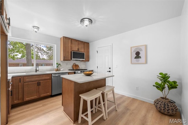 2736 Ashrock Dr, Saint Louis, MO 63129 - kitchen with a sink, appliances with stainless steel finishes, light wood-type flooring, a kitchen breakfast bar, and light countertops