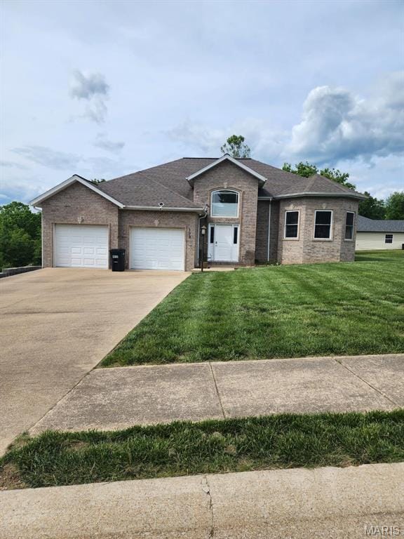 ranch-style home with concrete driveway, an attached garage, brick siding, a front lawn, and roof with shingles