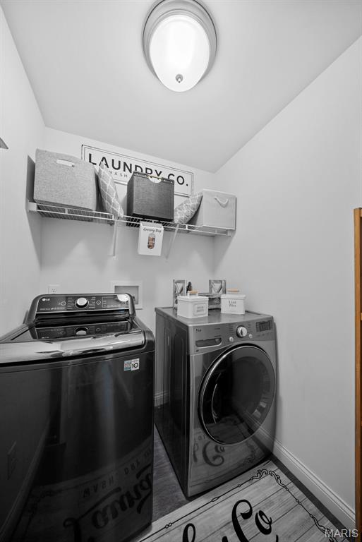 clothes washing area featuring separate washer and dryer, baseboards, and wood finished floors