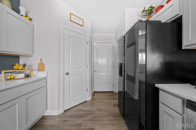 kitchen featuring freestanding refrigerator, dark wood-type flooring, light countertops, stainless steel dishwasher, and baseboards