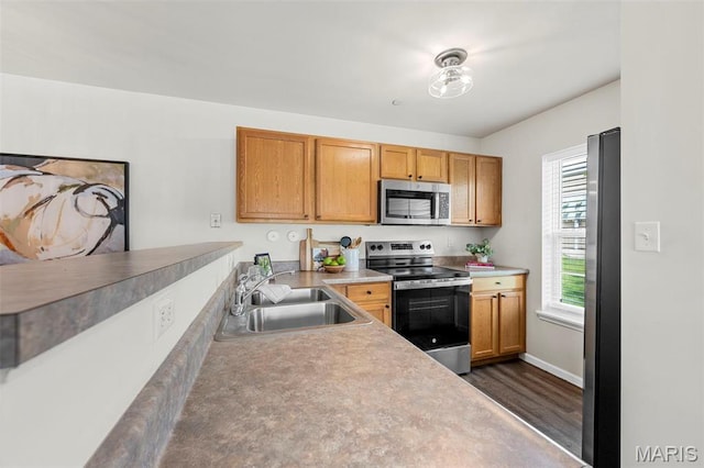 kitchen with appliances with stainless steel finishes, a sink, dark wood-type flooring, light countertops, and a peninsula
