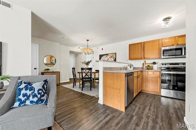 kitchen with appliances with stainless steel finishes, dark wood-style flooring, a chandelier, and light countertops