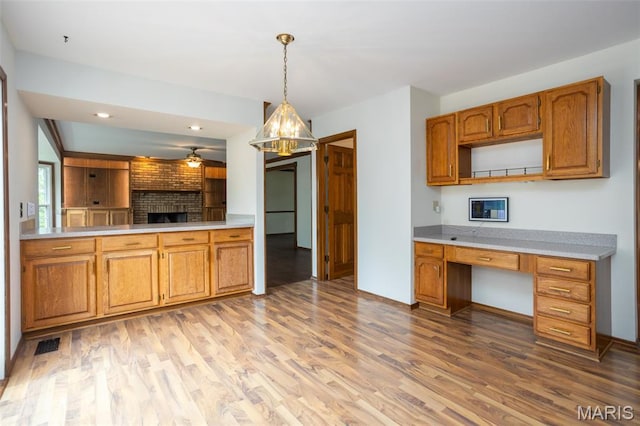 712 Carman Oaks Ct, Manchester, MO 63021 - kitchen with light wood-type flooring, brown cabinetry, light countertops, a fireplace, and pendant lighting