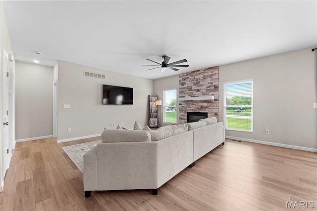 living area with a ceiling fan, baseboards, a fireplace, and light wood-style floors