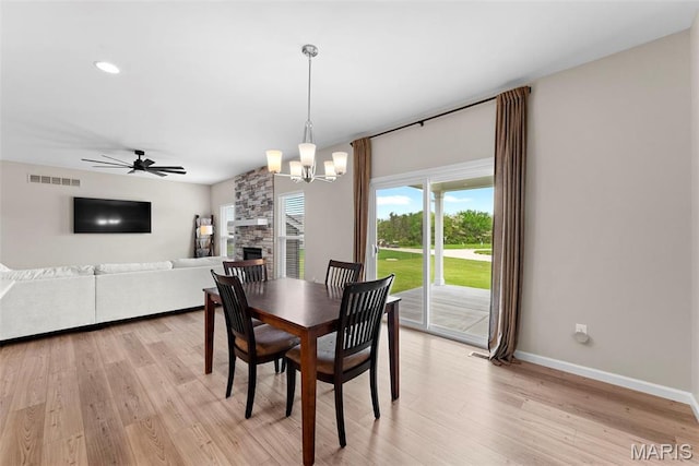 dining area with baseboards, light wood finished floors, a chandelier, a ceiling fan, and a stone fireplace