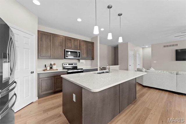 kitchen with stainless steel appliances, a sink, light wood finished floors, dark brown cabinets, and open floor plan