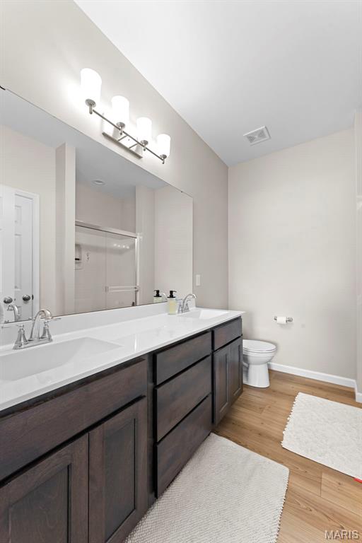 bathroom featuring wood finished floors, a stall shower, double vanity, toilet, and baseboards