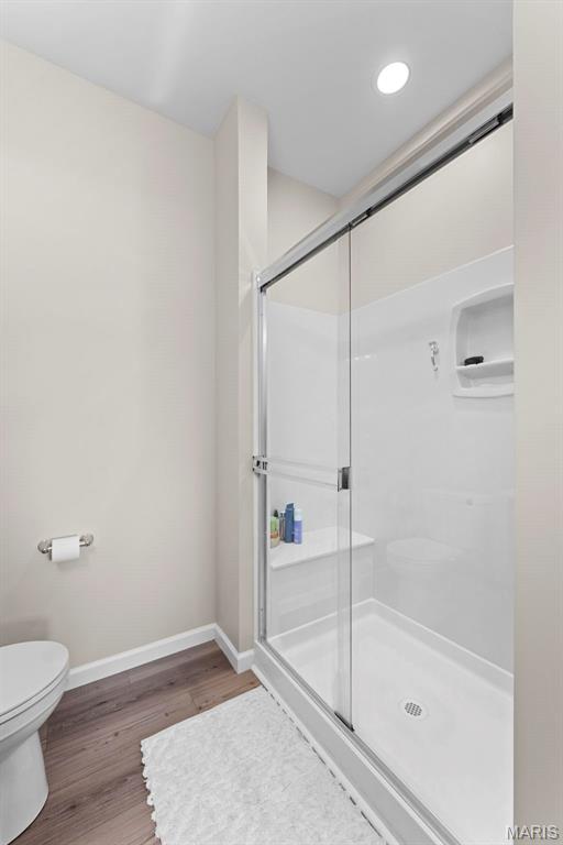 full bath featuring baseboards, a shower stall, toilet, and wood finished floors