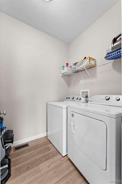 clothes washing area featuring separate washer and dryer, light wood finished floors, and baseboards