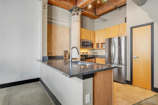 kitchen featuring appliances with stainless steel finishes, a sink, a peninsula, light brown cabinets, and dark stone counters
