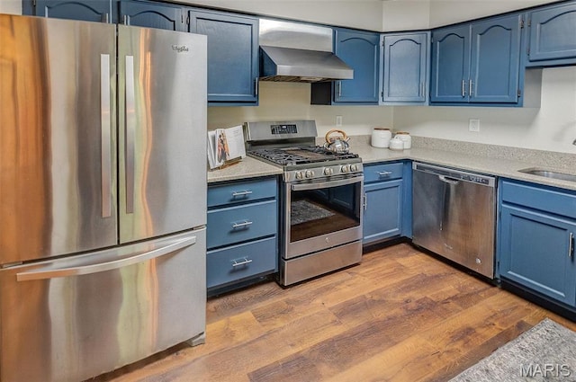 kitchen featuring appliances with stainless steel finishes, blue cabinets, and wall chimney range hood