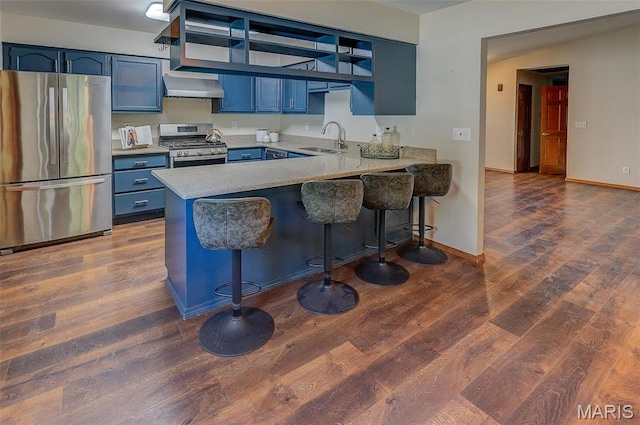 kitchen featuring appliances with stainless steel finishes, blue cabinets, wall chimney exhaust hood, a sink, and a peninsula