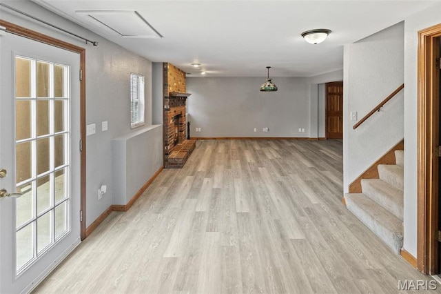 unfurnished living room featuring light wood-style flooring, healthy amount of natural light, a brick fireplace, and baseboards