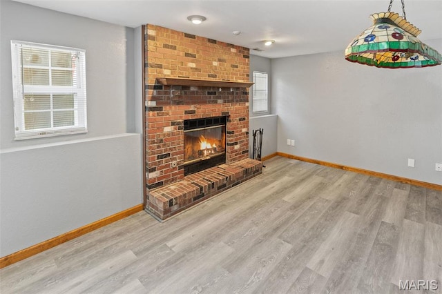 unfurnished living room with baseboards, wood finished floors, a brick fireplace, and healthy amount of natural light