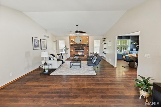 living area with wood finished floors, healthy amount of natural light, ceiling fan, a brick fireplace, and high vaulted ceiling
