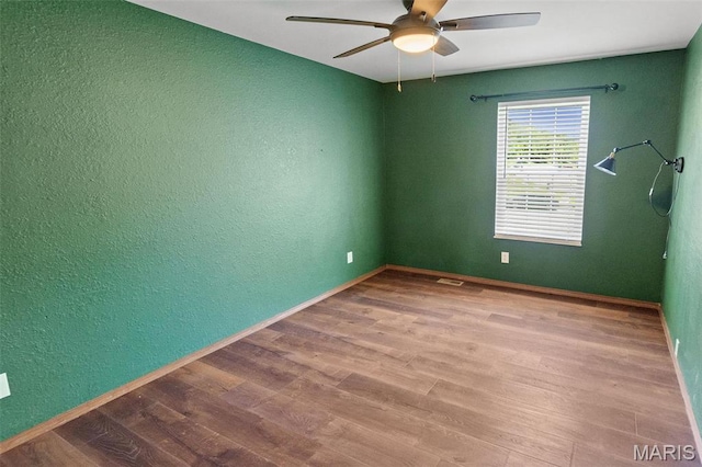 unfurnished room featuring a textured wall, a ceiling fan, wood finished floors, and baseboards