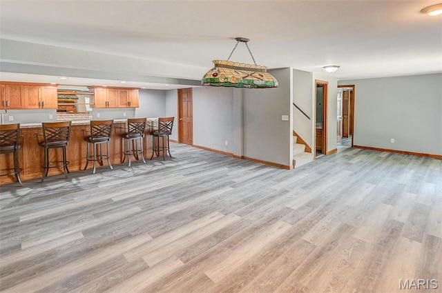 kitchen featuring light wood-style flooring, baseboards, a breakfast bar, and brown cabinetry