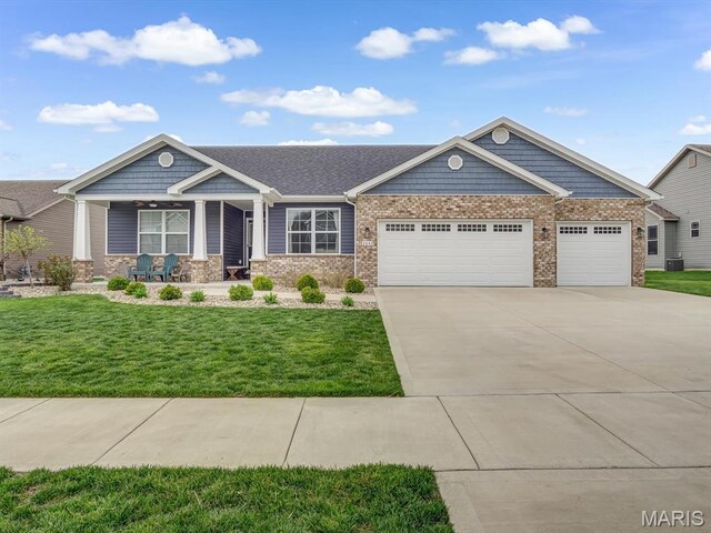 view of front of home featuring covered porch, an attached garage, driveway, a front lawn, and brick siding